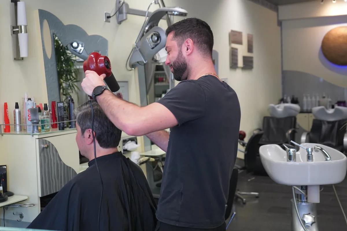 Man sieht einen Coiffeur am Haareföhnen.